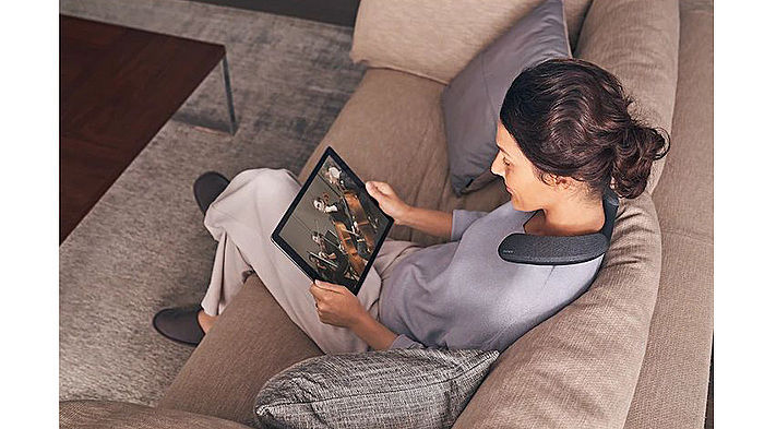 一名女子配戴Sony SRS-NS7 頸掛式揚聲器坐在沙發上觀看影片